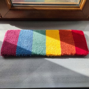 May include: A multi-colored striped rug with red, blue, green, yellow, orange, and purple stripes. The rug is made of a soft, fuzzy material.