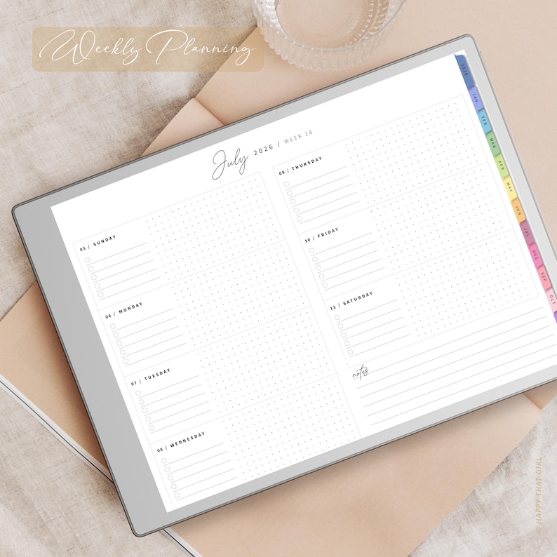 May include: A digital planner showing a weekly layout for July 2026. The screen displays a grid with days of the week, dotted sections, and the text "Weekly Planning." The planner has a colourful tabbed index and is set on a neutral surface.