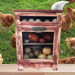 May include: A rustic, distressed red wooden cabinet with wire mesh doors and shelves, filled with eggs, tomatoes, and onions. The cabinet has a decorative handle and is set against a backdrop of green grass and chickens.