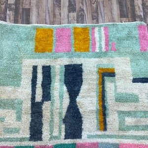 Op de afbeelding: Een kleurrijk abstract tapijt met geometrische vormen in tinten blauw, groen, geel, roze en wit. Het tapijt heeft een zachte, pluche textuur.