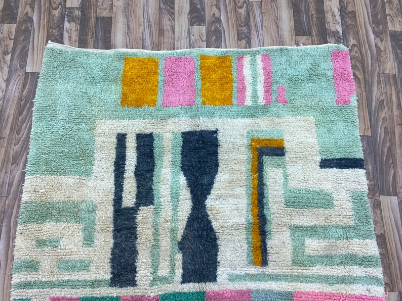 Op de afbeelding: Een kleurrijk abstract tapijt met geometrische vormen in tinten blauw, groen, geel, roze en wit. Het tapijt heeft een zachte, pluche textuur.