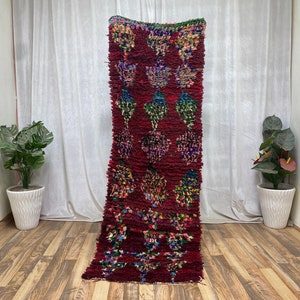Puede incluir: Una alfombra larga y rectangular hecha a mano con un fondo burdeos oscuro y patrones florales coloridos. La alfombra está hecha de un material texturizado y tiene una apariencia peluda. La alfombra mide aproximadamente 152 cm de largo.