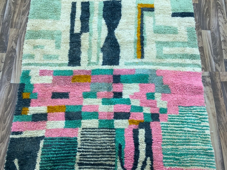 Op de afbeelding: Een kleurrijk tapijt met een geometrisch patroon in tinten roze, groen, blauw en geel. Het tapijt heeft een modern, abstract ontwerp.