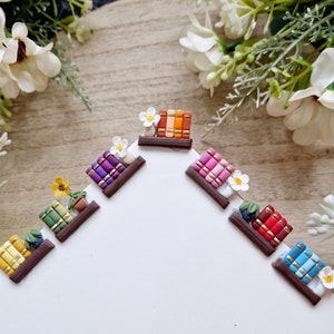 Könnte beinhalten: Ein Set mit sechs Miniatur-Bücherregal-Dekorationen mit verschiedenen farbigen Büchern und Blumen. Jedes Bücherregal ist aus braunem Ton gefertigt und verfügt über eine kleine Pflanze oder Blume.