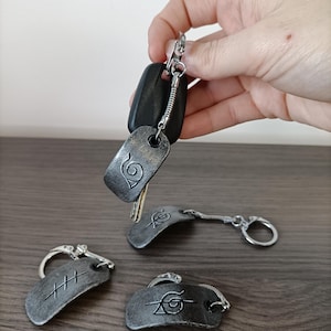 Peut inclure: Plusieurs porte-clés argentés avec des motifs gravés. L'un est attaché à des clés noires. Les porte-clés présentent divers symboles et sont présentés sur une surface en bois.