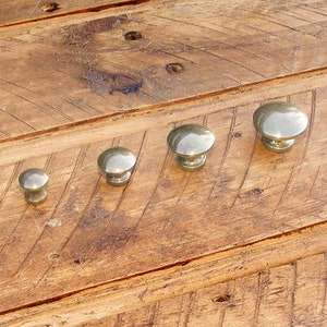 May include: Four silver metal cabinet knobs of varying sizes, arranged in a row on a wooden surface.