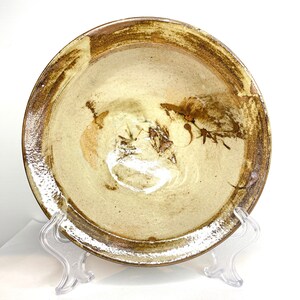 May include: A large, round, ceramic bowl with a brown rim and a light brown interior. The bowl has a subtle, abstract design in shades of brown and white.