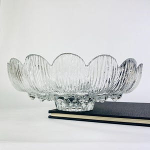 May include: A clear glass bowl with a scalloped edge and a textured, ribbed design. The bowl has a pedestal base.