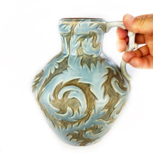 Puede incluir: Una jarra de cerámica azul y marrón con un patrón de remolino. La jarra tiene un asa y una boca ancha.