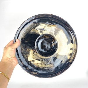 May include: A black ceramic serving dish with a smaller bowl in the centre. The dish has a speckled glaze with gold accents.