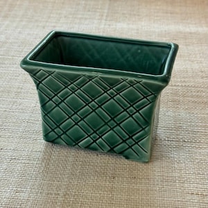 May include: A rectangular ceramic planter with a glossy dark green finish. The exterior features a raised, embossed lattice pattern consisting of intersecting diagonal lines that create a diamond grid texture across all visible sides of the vessel.