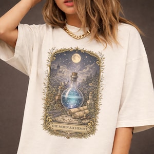 Puede incluir: Camiseta color crema con una ilustración detallada de un frasco de poción con tapón de corcho, sobre un cielo nocturno con luna llena. El diseño incluye otras botellas, pergaminos y el texto "THE MOON ALCHEMIST".