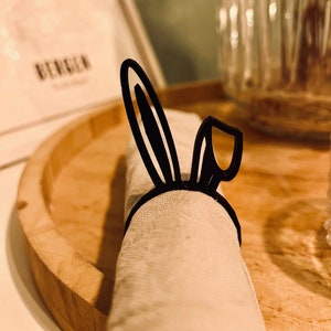 Könnte beinhalten: Schwarzer Hasen-Serviettenring aus Metall. Der Ring hält eine weiße Serviette.