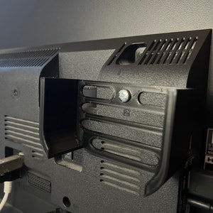 May include: Close-up of the back of a black television with various ports and connections. The television has a built-in stand with a textured surface.