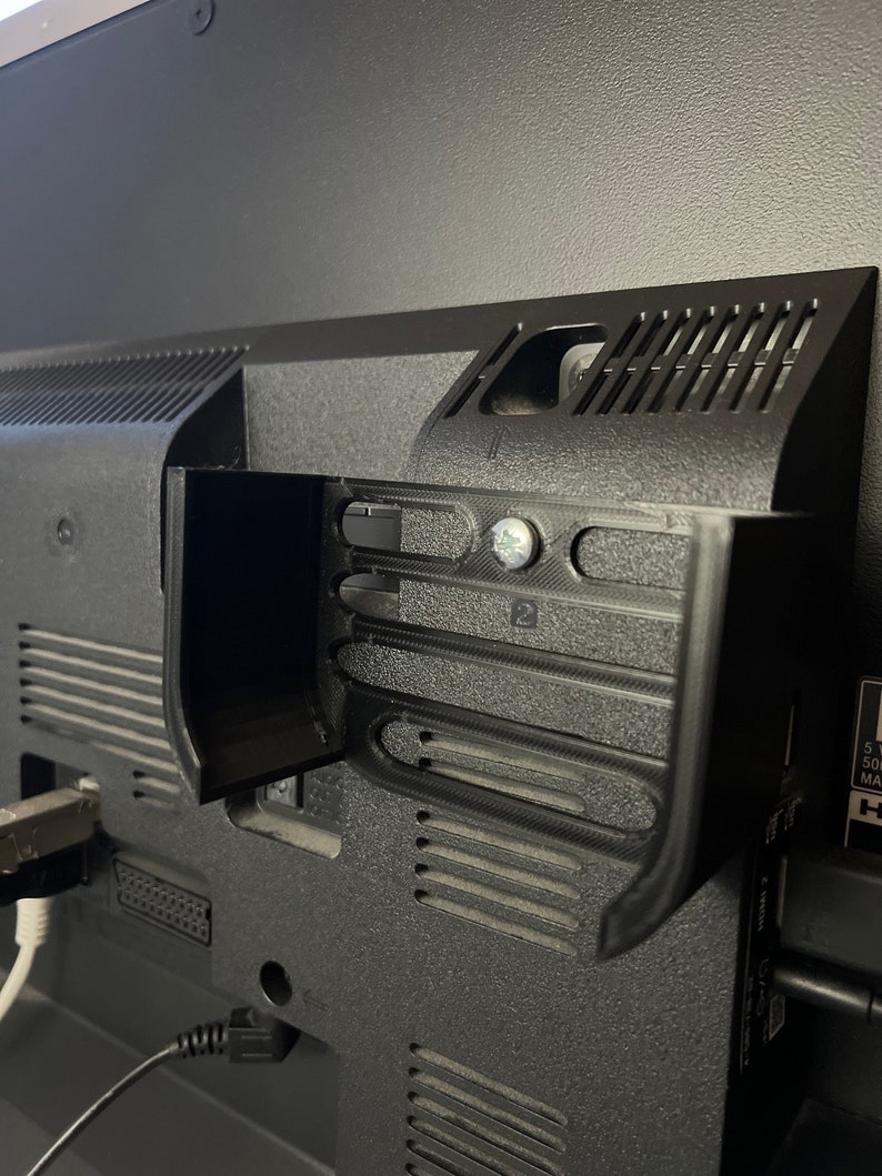 May include: Close-up of the back of a black television with various ports and connections. The television has a built-in stand with a textured surface.