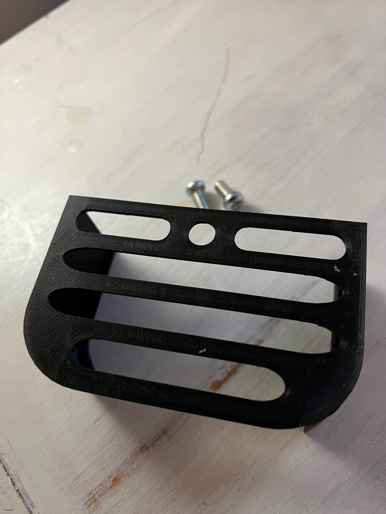 May include: A black plastic 3D printed shelf with four slots and a round hole in the center. Two silver screws are included.