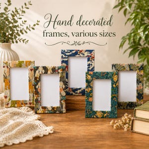 May include: Five hand-decorated picture frames of various sizes are displayed on a wooden surface. The frames feature colorful patterns, including floral and dog-themed designs. The text "Hand decorated frames, various sizes" is written above the frames.