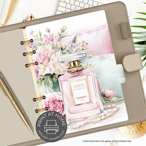 May include: A digital print featuring a pink perfume bottle with gold accents, labeled "COCO MADEMOISELLE CHANEL PARIS", set against a backdrop of watercolor flowers and a pearl necklace. The print is inside a tan binder with a gold pen.