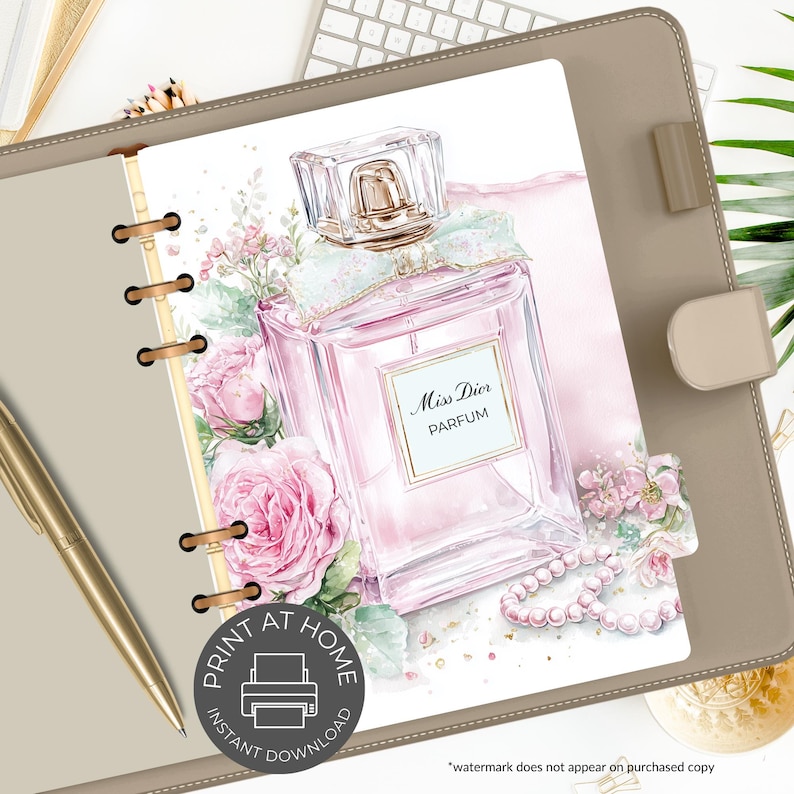 May include: A planner page featuring a watercolor illustration of a pink perfume bottle labeled "Miss Dior Parfum." The design includes pink roses, a pearl necklace, and a light blue bow. The page is inside a tan planner with a gold pen.