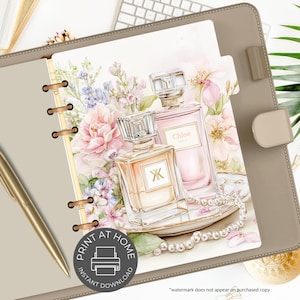 May include: A planner insert featuring two perfume bottles with floral accents and a pearl necklace. The bottles are in shades of peach and pink, with the word "Chlo&eacute;" visible on one. The insert is inside a tan planner with a gold pen.