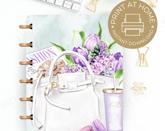 May include: A printable planner page featuring a white handbag, a purple and white floral bouquet, a purple tumbler with a gold lid and straw, and two purple macarons. The text "FASHION" is visible on a magazine in the background.