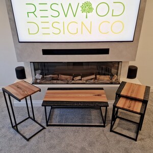 May include: A set of three tables featuring natural wood grain tops with dark, textured resin edges and black metal frames. The set includes one rectangular coffee table and two smaller side tables, all displaying a consistent design aesthetic.