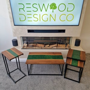 May include: A set of three tables featuring natural wood tops with a central green resin inlay and black metal frames. The set includes one rectangular coffee table and two smaller side tables, one of which is a C-shaped table.