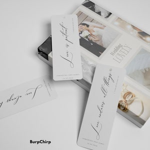May include: Three white bookmark tags with black calligraphy. The text on the tags reads "Love is patient", "Love endures all things", and "Love endures all things". The tags are for a wedding and include the couple's names and wedding date.