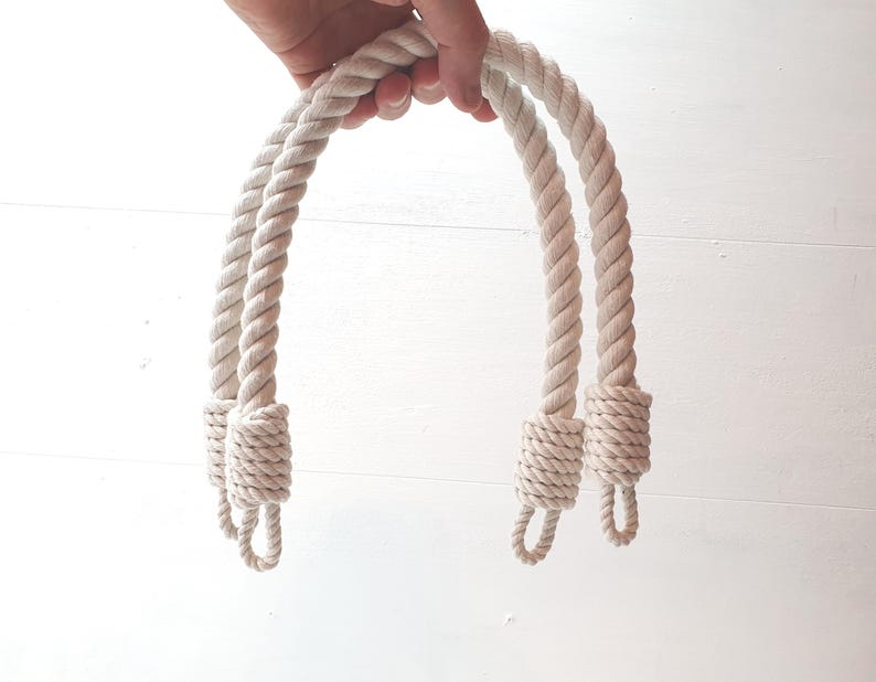 Op de afbeelding: Twee cr&egrave;mekleurige touwhandvatten voor een tas of mand. De handvatten zijn dik en gedraaid, met decoratieve knopen aan de uiteinden. Het touw heeft een neutrale kleur, geschikt voor diverse knutselprojecten.