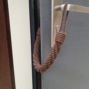 May include: A brown rope doorstop hanging on a door handle. The doorstop is made of a thick, braided rope and has a loop at the top.