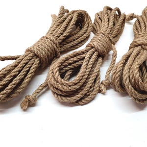 Puede incluir: Tres carretes de cuerda de yute natural de color marrón. La cuerda es gruesa y tiene una textura rugosa.