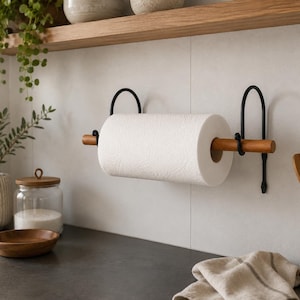 May include: A wall-mounted paper towel holder featuring two black metal brackets with arched tops and a smooth, cylindrical wooden rod that holds a single roll of white paper towels. The design is functional and minimalist in its construction.