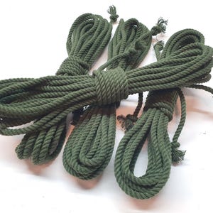 May include: Four spools of green cotton rope, each wound into a tight coil. The rope is a dark green color and has a rough texture.