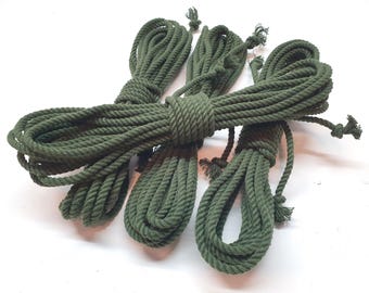 May include: Four spools of green cotton rope, each wound into a tight coil. The rope is a dark green color and has a rough texture.