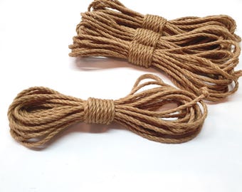 May include: Two spools of natural brown twine rope. One spool is coiled and the other is laid out in a straight line.
