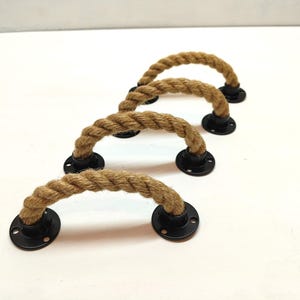 Puede incluir: Cuatro tiradores de armario de cuerda marrón con bases de metal negro. La cuerda está trenzada y las bases son redondas.