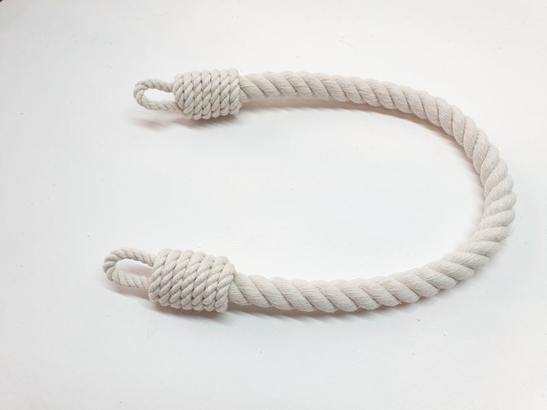Op de afbeelding: Een cr&egrave;mekleurige touwhandgreep met een lus aan elk uiteinde. Het touw is strak gedraaid en de uiteinden zijn geknoopt om een veilige lus te vormen. De handgreep is ontworpen voor gebruik op een tas of ander item.