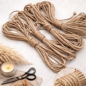 Può includere: Quattro fasci di corda di iuta color naturale, ben avvolti e legati. La corda è di colore marrone chiaro, con una consistenza leggermente ruvida. L'immagine include anche una candela accesa in un contenitore d'argento, forbici ed erba decorativa essiccata.