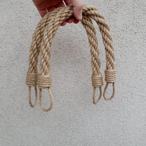 Könnte beinhalten: Drei natürliche Faserseilgriffe mit geknüpften Enden. Die Griffe sind geflochten und haben eine natürliche beige Farbe.