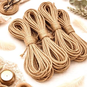 May include: Four bundles of natural jute rope, tightly wound and secured with twine. The image also includes a pair of vintage scissors, a candle, feathers, and decorative lace, suggesting a craft or home decor theme.