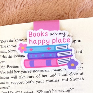 May include: A pink and purple bookmark with a stack of books and the text "Books are my happy place".
