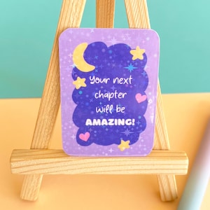May include: Purple sticker with a sparkly background and a cloud with stars and a crescent moon. The text reads "Your next chapter will be AMAZING!"