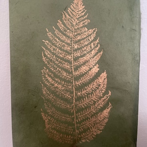 May include: A green paper card with a gold fern leaf design. The fern leaf is pressed into the paper and has a raised texture.