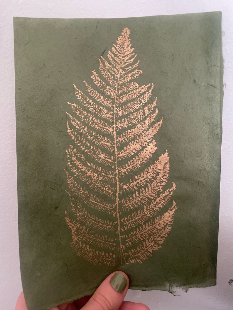 May include: A green paper card with a gold fern leaf design. The fern leaf is pressed into the paper and has a raised texture.