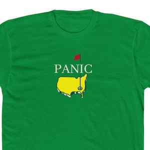 May include: Green t-shirt with the word "PANIC" above a yellow and green golf course map graphic. The graphic includes a red flag. The shirt is a solid green color.