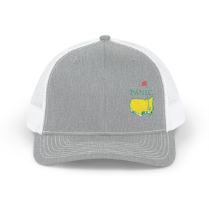 May include: A gray trucker hat with a white mesh back. The front of the hat features the word "PANIC" above a green and yellow map graphic with a red flag. The hat has a curved brim and a snapback closure.