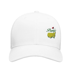 Peut inclure: Casquette de baseball blanche avec un patch brodé vert et jaune qui dit "Panic" et un drapeau rouge.