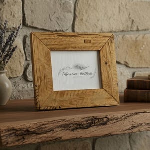 Puede incluir: Un marco de fotos cuadrado de madera rústica con una inserción blanca con texto. El marco está hecho de madera clara texturizada y se encuentra sobre una estantería de madera. Un pequeño jarrón con lavanda y libros también están en el estante.