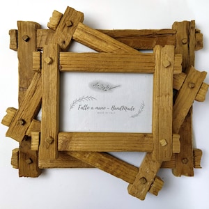 Può includere: Una cornice rustica in legno con un design unico e stratificato. La cornice è costruita con pezzi di legno marrone chiaro, tagliati grossolanamente, assemblati con perni visibili. Il centro presenta un inserto bianco con il testo "AnStyle" e "Fatto a mano - Handmade MADE IN ITALY".