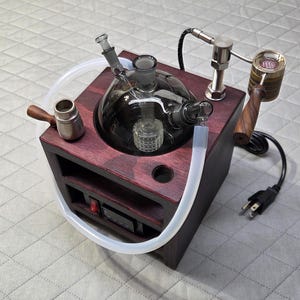 Puede incluir: Un dispositivo de escritorio de madera roja oscura con un globo de vidrio central con percolador, un cuenco de metal con mango de madera, un elemento calefactor con mango de madera, una manguera de silicona transparente, cable y panel de control.
